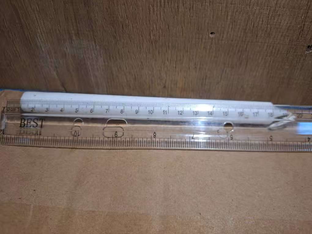 White taper candle shown horizontally against a ruler for length reference